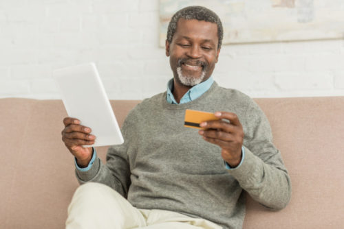 A man holding a tablet in one hand and his credit card in the other.