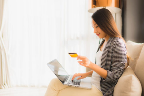 A woman online shopping while holding her credit card.