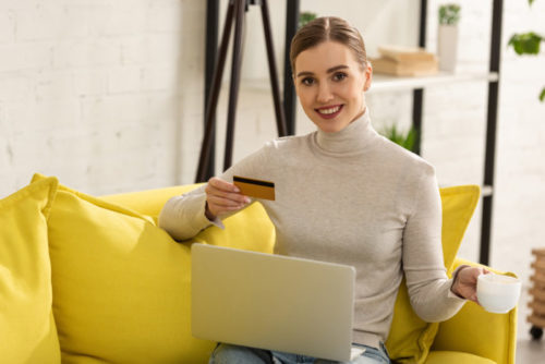 A smiling woman holds coffee and her credit card while shopping online.
