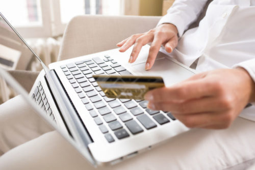 A woman shopping online with her credit card in one hand.