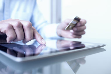 A man using a tablet while holding a credit card.
