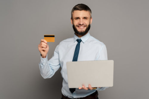 A businessman holding a laptop and his credit card.