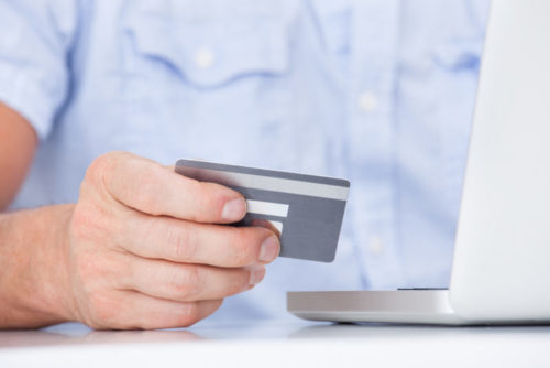A closeup of a man holding a credit card while on his laptop.