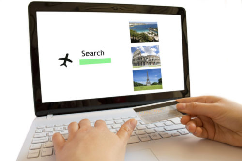 A man holds his credit card while booking a flight online.