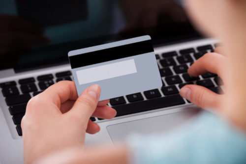 A close up of a woman holding her credit card over her laptop keyboard.