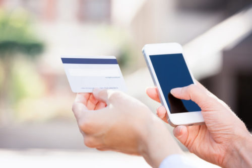 A woman holds her cell phone in one hand and a credit card in the other.