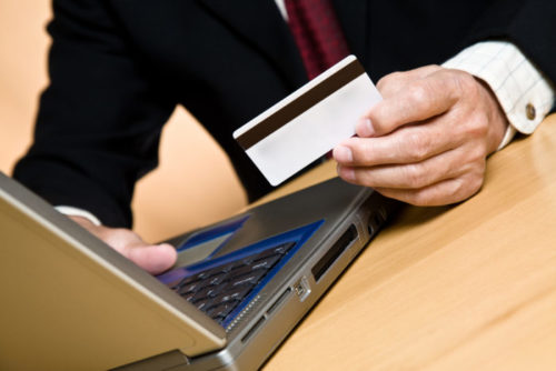 A person in business attire shopping on their laptop while holding a credit card.