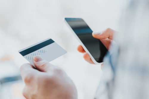 A close up of a man holding his credit card in one hand and his phone in the other.