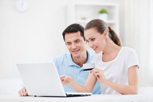 The woman of a smiling couple holds a credit card while pointing at a computer screen.
