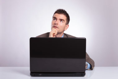 A person sits at a desk, in deep thought behind a laptop.