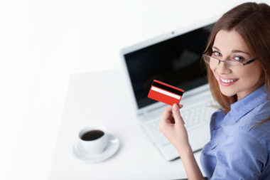 A person working on a laptop while drinking coffee and holding a credit card.