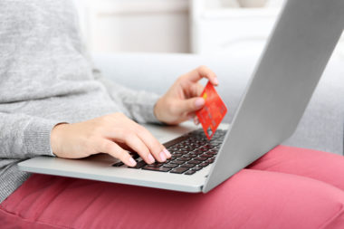 A person sitting while holding their laptop on their lap and holding a credit card.