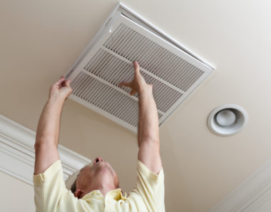 A person installing a central air conditioning vent in their home.