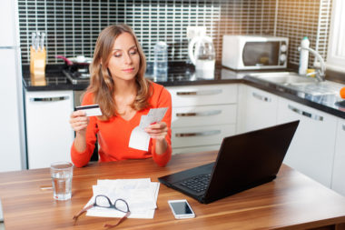 A person holding a bank card while examining financial statements with a computer in front of them.