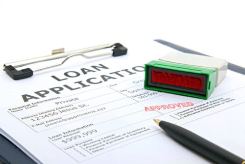 A pen sits on top of a loan application that is rubber stamped "approved."