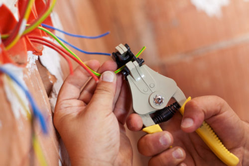 An electrician peeling the wires of a house with a tool.