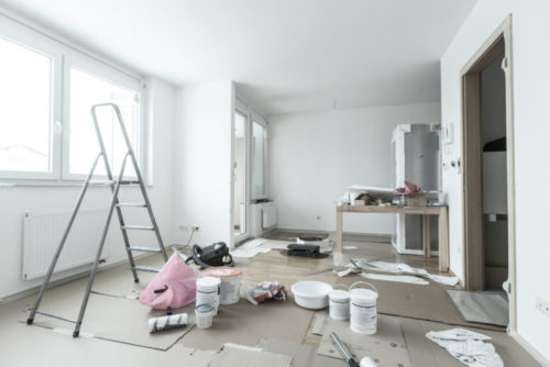 A stripped down room has home improvement tools and materials scattered throughout it.