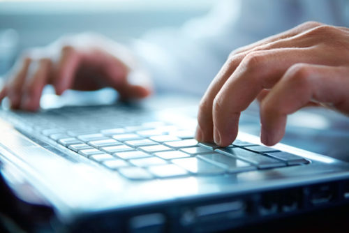 A closeup of a person's hands typing a letter on their laptop.