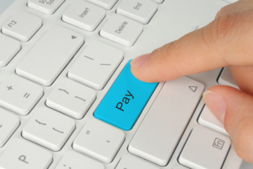 A closeup of a hand poised to press a blue "pay" button on a white keyboard.