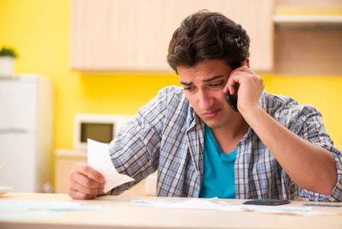 A worried person speaking on the phone while holding an invoice.