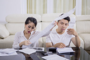 A worried couple calculating their debt, using receipts and a calculator.