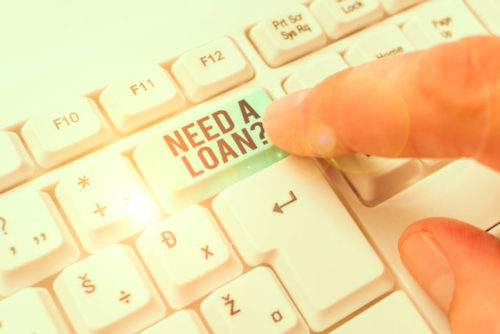 A closeup of a finger poised to press a button on a computer keyboard that reads "need a loan?"