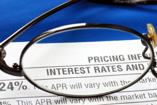 An eyeglass lens focuses on the words on the top of a document that reads "interest rates."