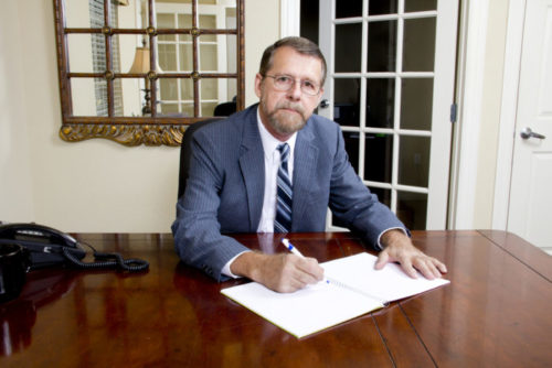 A loan officer looks at the camera while writing in a notebook at their desk.