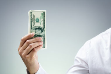 A loan officer holds up a stack of $100 bills.