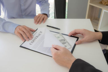 A loan officer hands a person a contract with loan money in it.