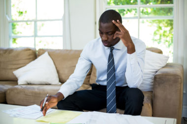 A person looks worried when examining financial documents on their couch.