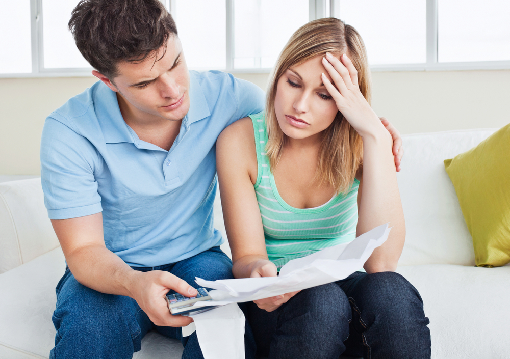 A worried couple sit on the couch examining financial documents.