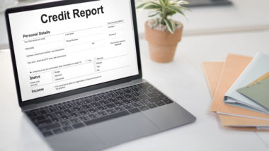 A laptop's screen reads "credit report" while sitting on a desk next to some folders.
