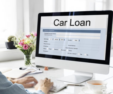 A person sitting down to their computer, which displays a car loan application screen.