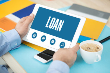 A person holding a tablet at their coffee table with a screen that reads "loan."