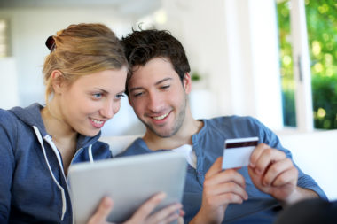 A couple shopping online. One partner holds a credit card while the other holds a mobile device.