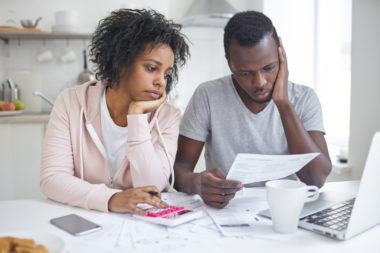 A couple looks stressed while reviewing their finances in their kitchen.