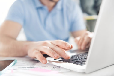 A person working on their laptop with financial documents on their desk.