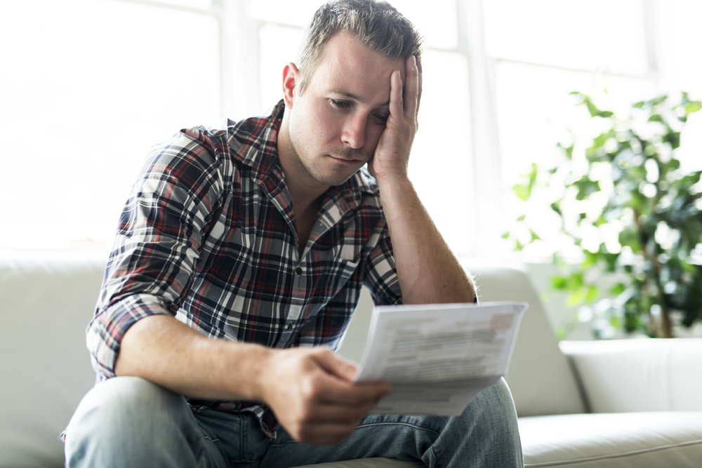 A person looking worried as they examine financial documents on their couch.