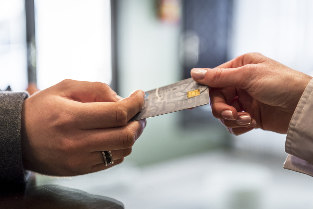 A closeup of a person handing a credit card to a clerk.