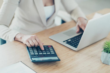 A person typing on their laptop while calculating their finances.