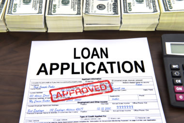 A loan application is rubberstamped "approved" next to stacks of cash.
