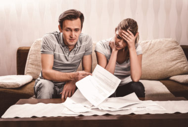 A worried couple on the couch going through financial documents.