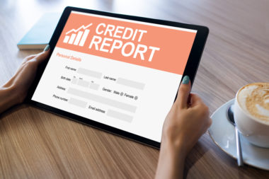 A person holds a tablet, whos screen reads "credit report."