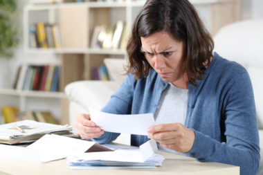 A confused woman looking at a check in her home, confused as to why it was declined.