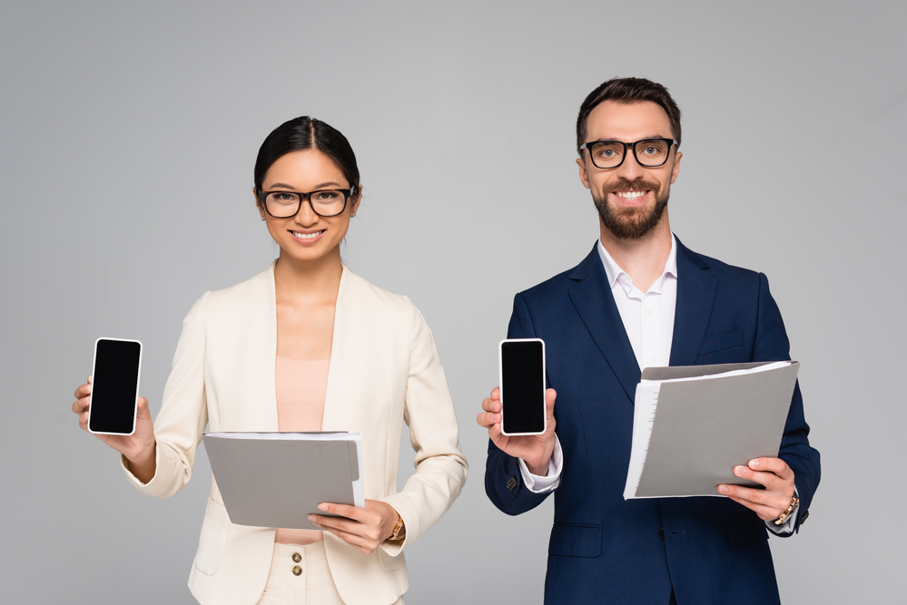 Two professionals holding a folder in one hand and a phone in the other.