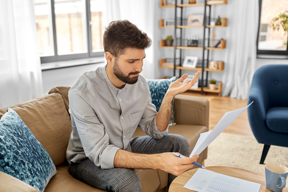 A person throws a hand up in frustration while looking at financial documents.