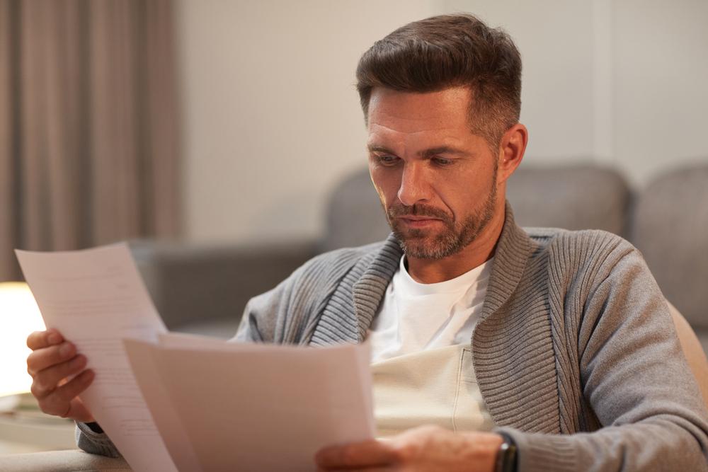 A person examining financial document on their couch.