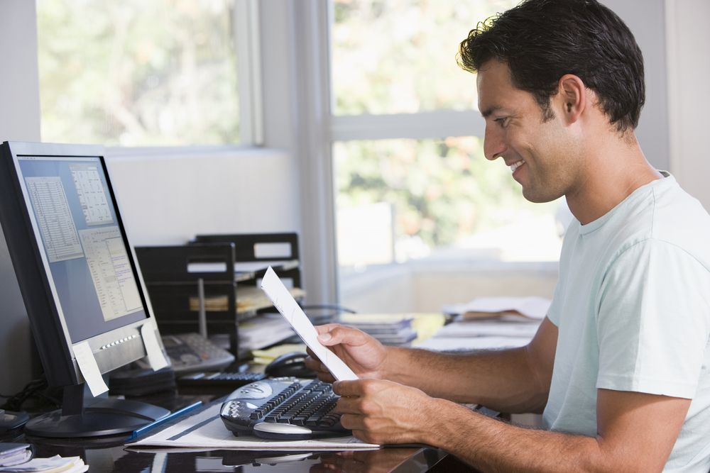 A person smiles while reading a financial document in front of their computer.