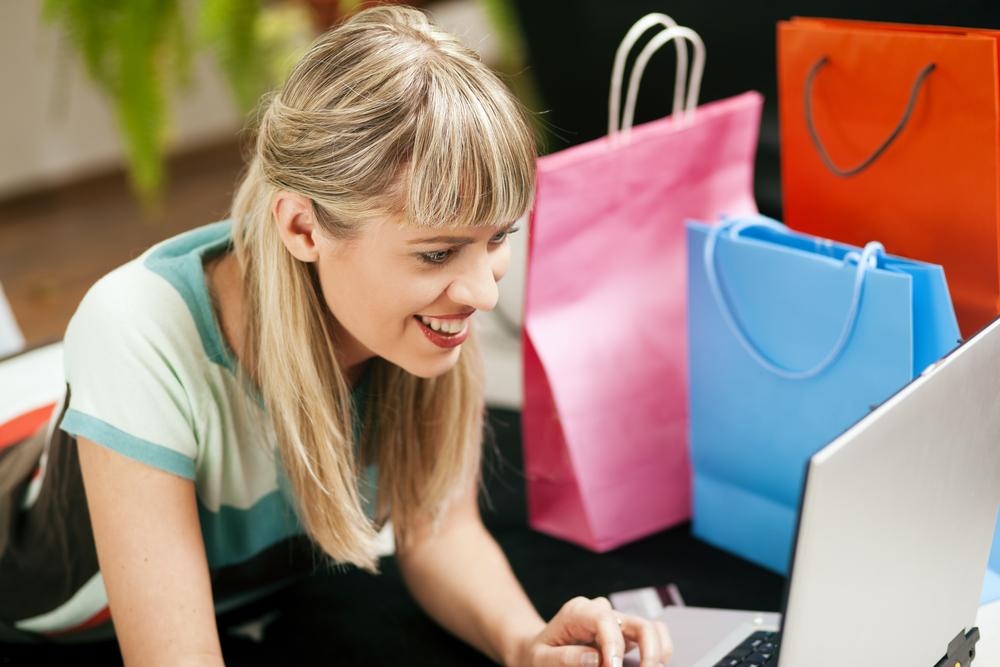 A person shopping online with shopping bags next to her.